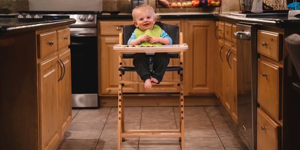 baby in green shirt sitting on brown wooden high chair