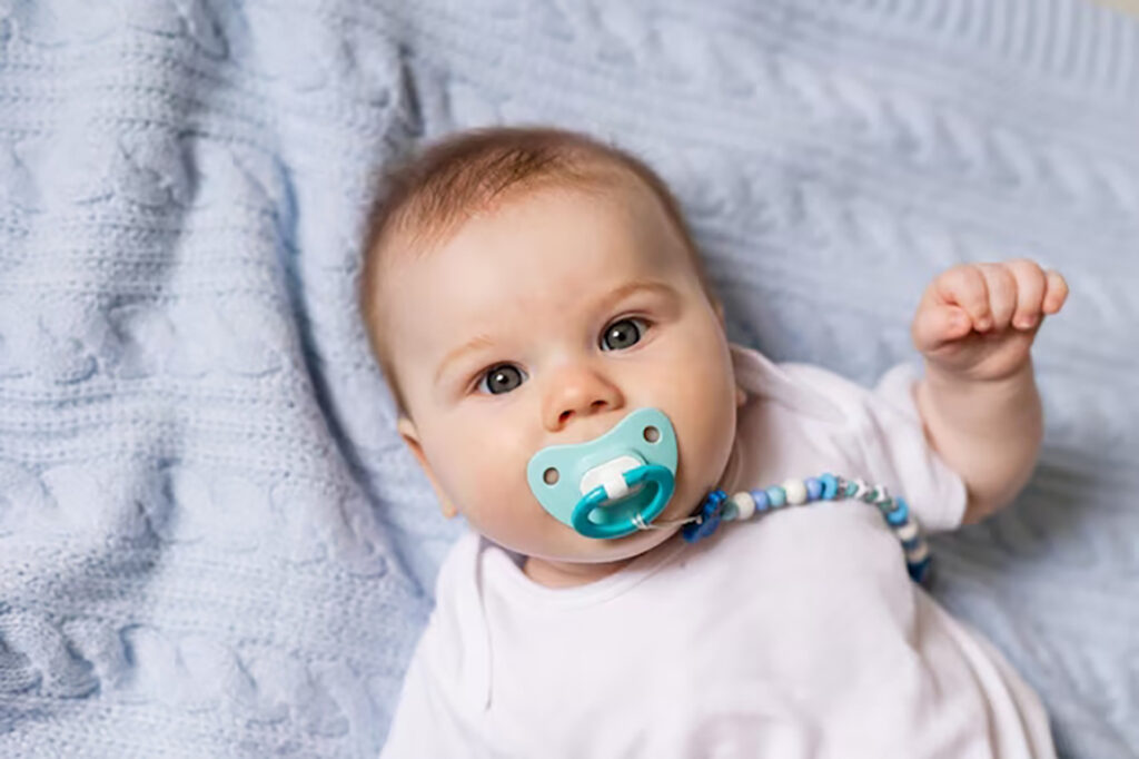 Chupeta para Recém-Nascido: Como escolher a melhor em 2025 1 retrato de bebe recem nascido fofo com uma chupeta na boca deitado de costas no cobertor de malha az