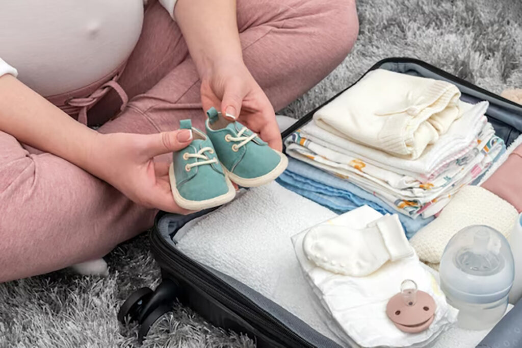Kit Bolsa Maternidade: O Essencial para a Chegada do Bebê 2 mulher gravida segurando sapatos de bebe e embalando saco de maternidade mae durante a gravidez espe