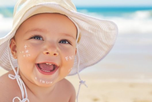 Bebê feliz na praia com protetor solar.